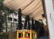 Beige retractable awnings installed above a landscaped outdoor playground with a green slide