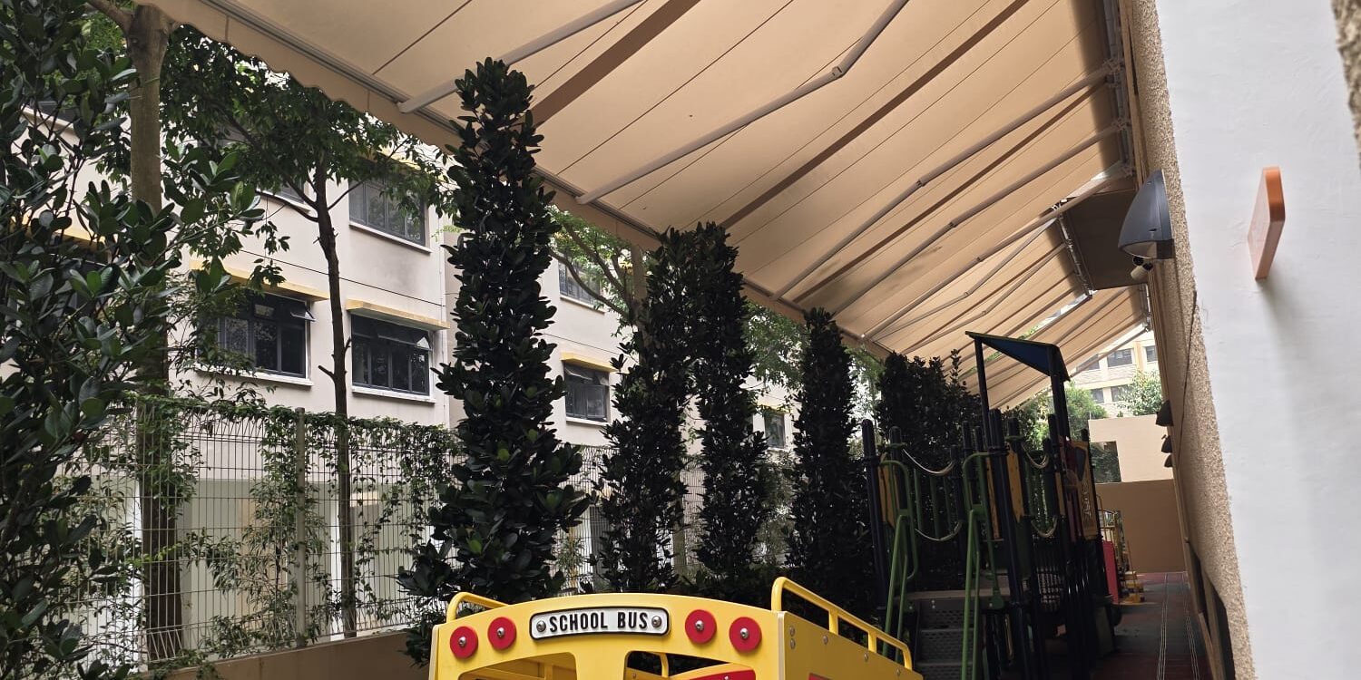 Beige retractable awnings installed above a landscaped outdoor playground with a green slide