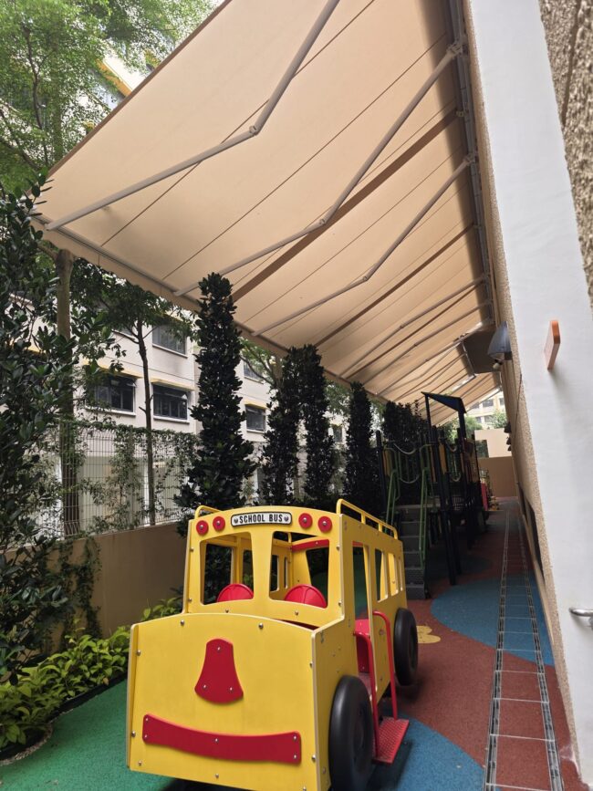 Beige retractable awnings installed above a landscaped outdoor playground with a green slide