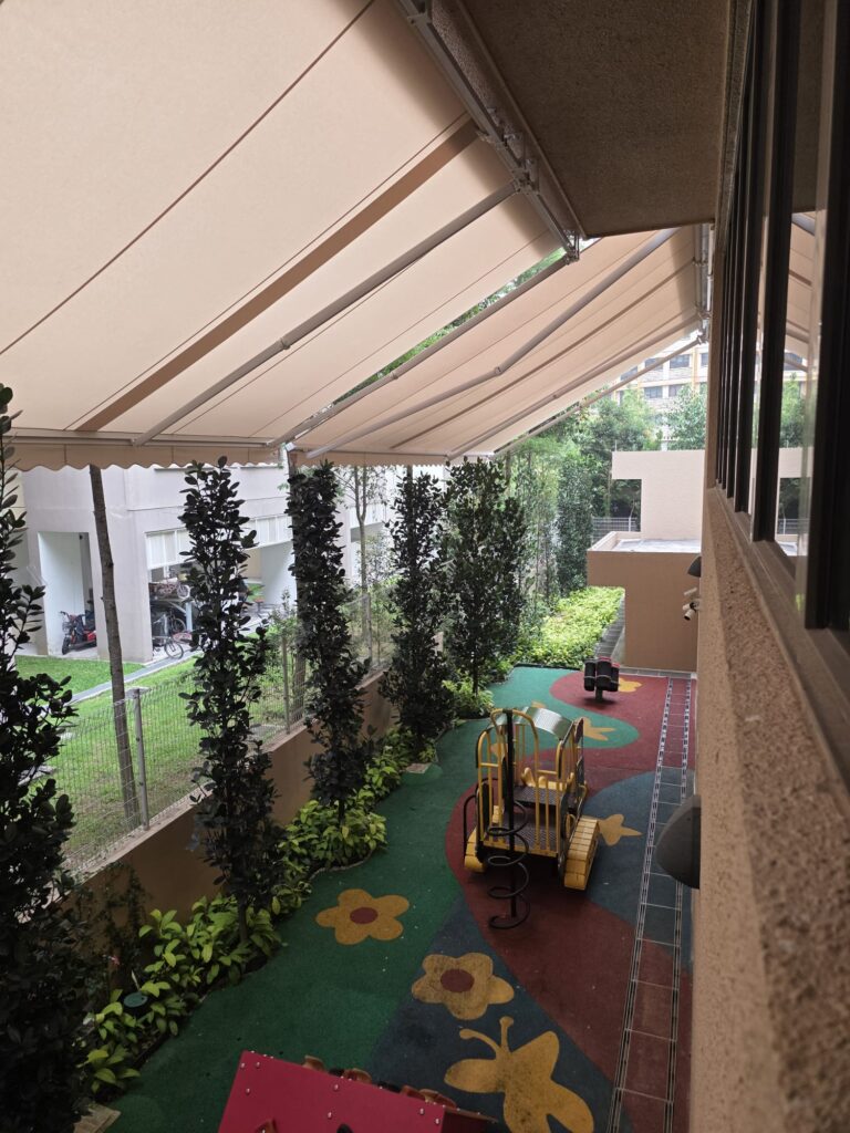 Extended beige retractable awnings shading a narrow outdoor play area with colourful flooring