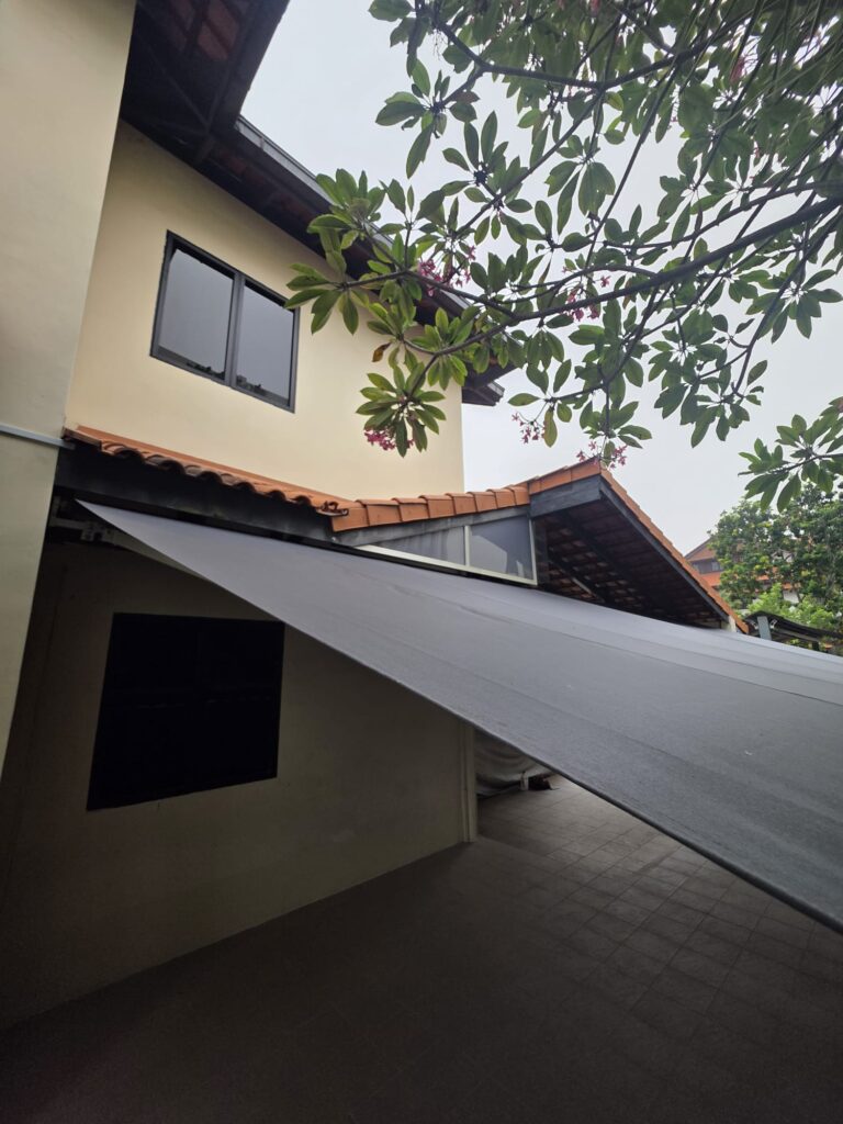 Extended black retractable awning covering the tiled walkway beside a house