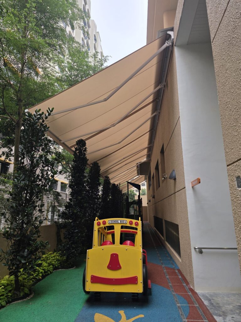 Wall-mounted beige retractable awnings extending over a children's play area beside a building